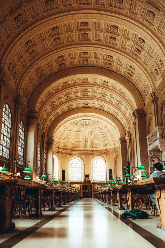 Students studying at long tables under green lamps in Bates Hall at the Boston Public Library.